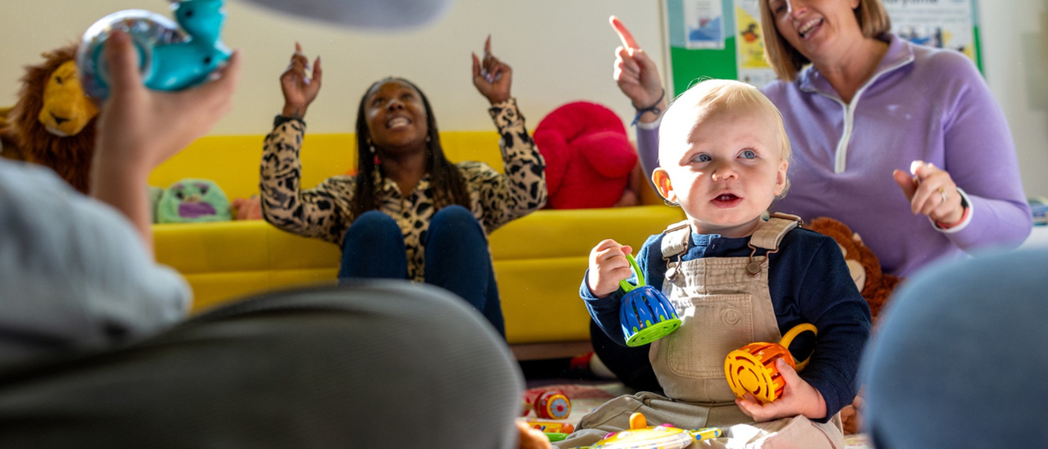 A young child taking part in a childcare activity with two adults behind them