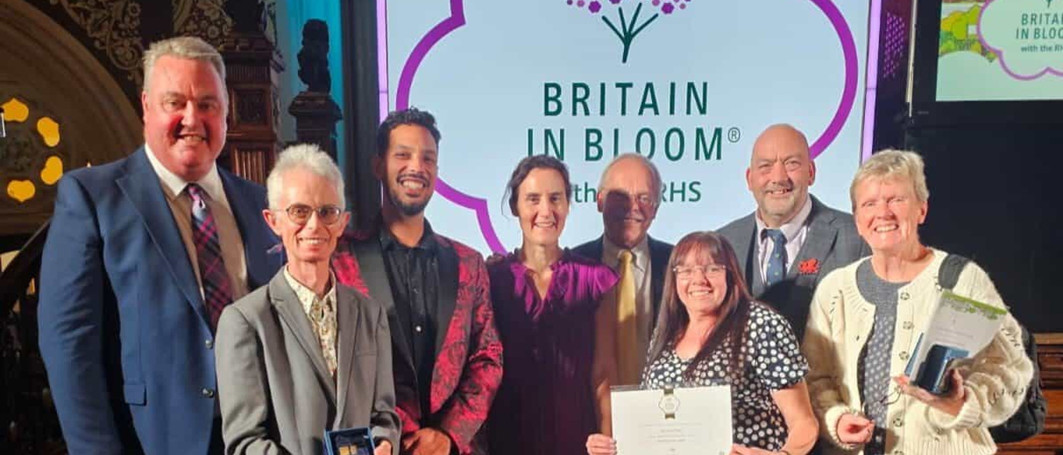 Wrexham Council representatives and volunteers holding awards in front of a Britain in Bloom screen at the finals ceremony in Rochdale. Photo: Wrexham Council