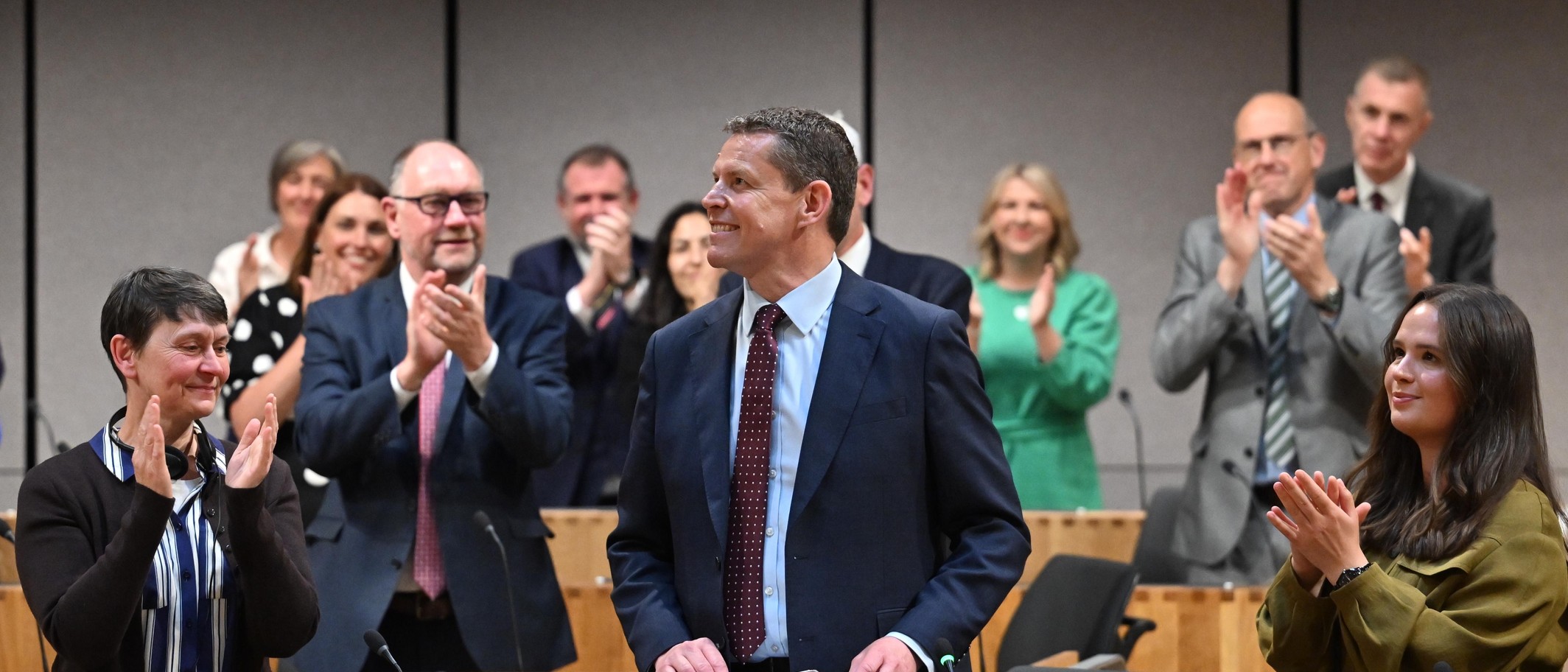 Archive photograph of Rhun ap Iorwerth in the Senedd chamber on 12 May 2026, with members applauding around him. Photo: Senedd Cymru / Welsh Parliament, CC BY 4.0; cropped.